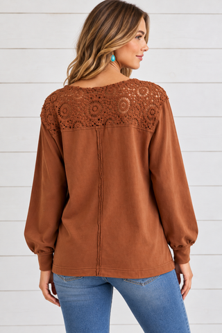 Back view of a rust long-sleeve top featuring a floral crochet upper-back panel and exposed center seam.