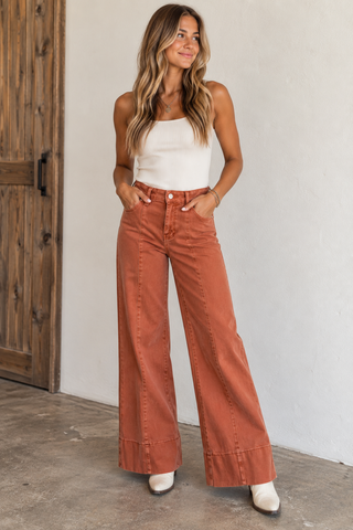 Model wearing rust washed high-rise wide-leg jeans with front seam detailing and wide hem.