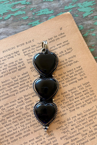 Three black onyx heart stones stacked vertically in a silver-tone alloy pendant with textured borders and decorative bead details.