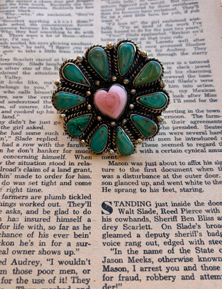 Turquoise statement ring featuring teardrop-shaped turquoise stones arranged in a flower design around a pink heart-shaped center stone, finished with ornate silver-tone detailing.