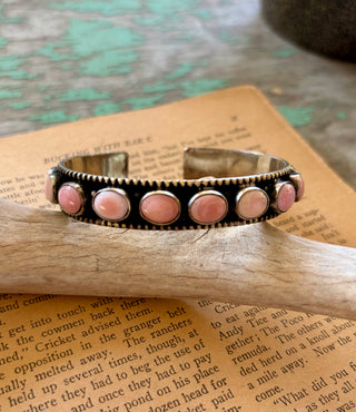 Adjustable silver-tone alloy cuff bracelet with round pink conch accents, an antiqued finish, and beaded edges.