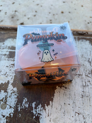 Orange pumpkin squishy with a black smiling jack-o’-lantern face and green stem on a distressed wood surface.