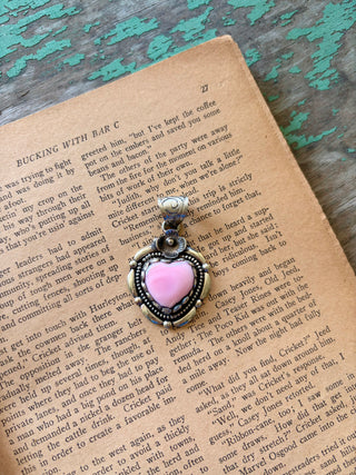 Pink heart-shaped pendant with an antiqued silver-tone setting, beaded border, and small flower accent above the stone.