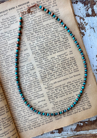 22-inch necklace with alternating Cloud Mountain turquoise beads and copper beads, displayed on an open book.