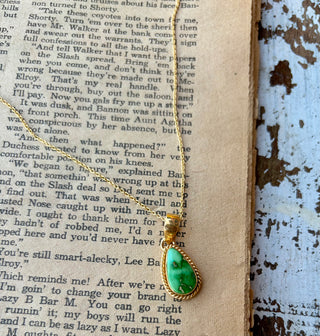 Green Sonoran Gold turquoise teardrop pendant with a gold rope-style border on a gold-plated sterling silver chain, displayed on an open book.