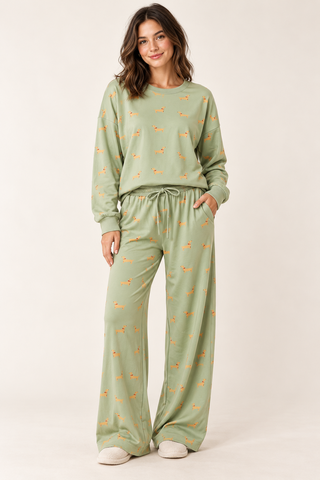 Model wearing a sage green dachshund\-print lounge set with a long\-sleeve crewneck top and wide\-leg drawstring pants\.