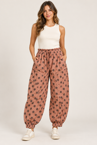     Model wearing dusty rose balloon pants with brown polka dots, a drawstring waist, and front pockets.