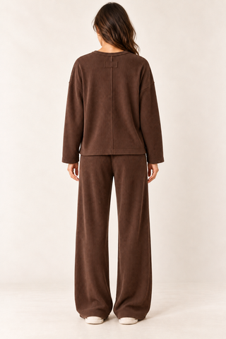 Model wearing a brown waffle knit lounge set with a long-sleeve crewneck top, chest pocket, and matching wide-leg pants.