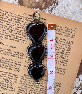 Three black onyx heart stones stacked vertically in a silver-tone alloy pendant with textured borders and decorative bead details.