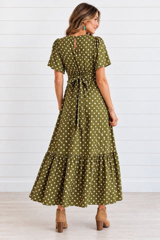 Model wearing an olive green polka dot maxi dress with flutter sleeves and a ruffled hem, styled with tan ankle boots.