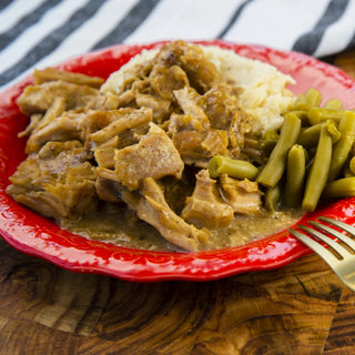 Crockstar Southern Style Pork Chops in gravy with mashed potatoes and green beans, served on a red plate.