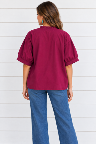 Back view mockup of a model wearing a relaxed berry blouse with gathered sleeve cuffs and blue jeans.