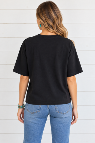 Back view of a female model wearing a plain black relaxed tee with denim jeans.