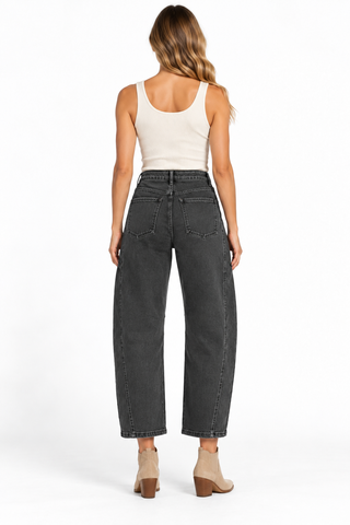 Model wearing washed black barrel jeans with curved knee seams, a cream tank top, and tan ankle boots.