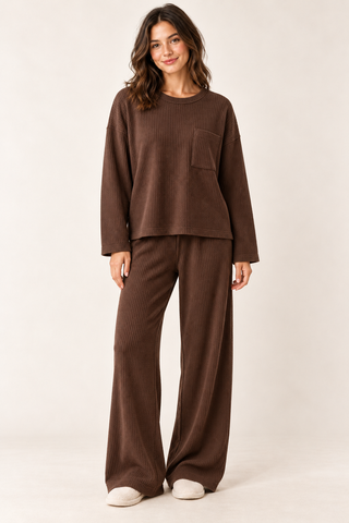 Model wearing a brown waffle knit lounge set with a long-sleeve crewneck top, chest pocket, and matching wide-leg pants.