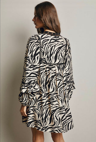 A woman wearing a black and beige zebra-print long-sleeve dress, shown from the back against a plain light gray studio background.