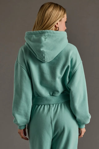 A woman shown from the back wearing a matching mint green hooded sweatshirt and jogger pants set against a solid gray studio background.