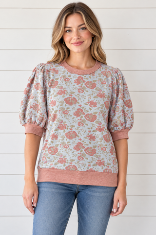 Front view of a model wearing a blue-gray floral puff sleeve top with dusty rose ribbed trim and jeans.