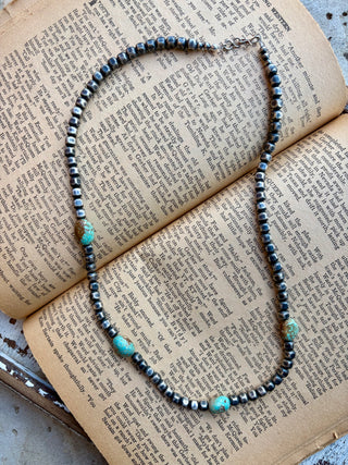 22-inch necklace with 5 mm sterling silver box pearls and authentic turquoise accents displayed on an open book.