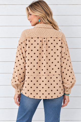 Back view of a tan gauze shirt with brown polka dots, a small-dot shoulder panel, and exposed horizontal seams, worn with jeans.