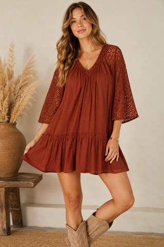 Woman wearing a rust mini dress with crochet lace sleeves and a tiered ruffle hem