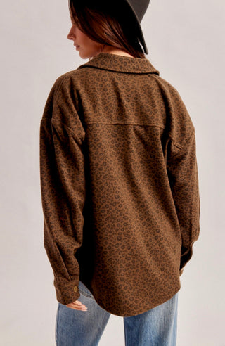 A woman shown from the back wearing a brown leopard-print button-up shirt and blue jeans against a plain light gray studio background.