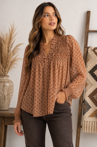 Mocha brown polka dot blouse with ruffle neckline, smocked detailing, sheer long sleeves, and a flowy feminine fit.