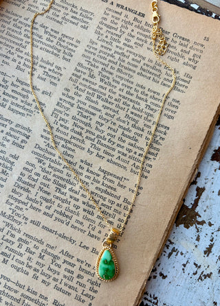 Green Sonoran Gold turquoise teardrop pendant with a gold rope-style border on a gold-plated sterling silver chain, displayed on an open book.