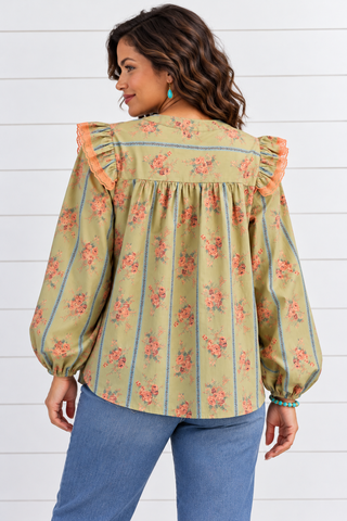 Back view of a sage green floral blouse with blue stripes, lace-trimmed shoulder ruffles, and a gathered back, worn with jeans.