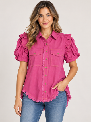     Model wearing a magenta button-up top with ruffle shoulders, puff sleeves, chest pockets, and a frayed hem.