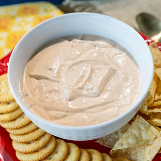 Crockstar Fiesta Mexican Dip in a white bowl surrounded by round crackers and tortilla chips on a red platter.