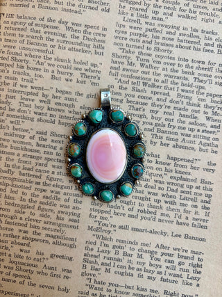 silver pendant featuring a large oval pink conch shell center surrounded by natural turquoise stones in an ornate Southwestern setting.
