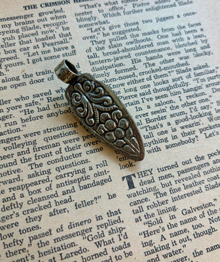 Handcrafted black onyx arrowhead pendant with a genuine turquoise accent set in an antique silver alloy setting, displayed on a vintage book background.