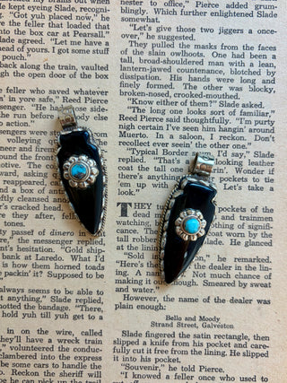 Handcrafted black onyx arrowhead pendant with a genuine turquoise accent set in an antique silver alloy setting, displayed on a vintage book background.