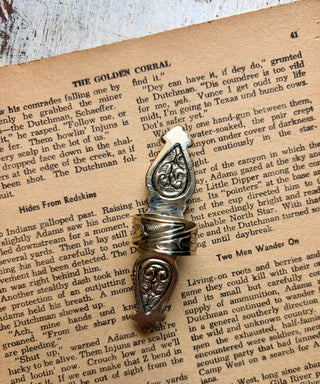 A silver-toned metal ring with an ornate scrollwork design, resting on an open book page with printed text.