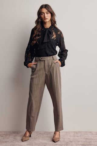 Woman wearing a black lace blouse and brown plaid pants against a plain background