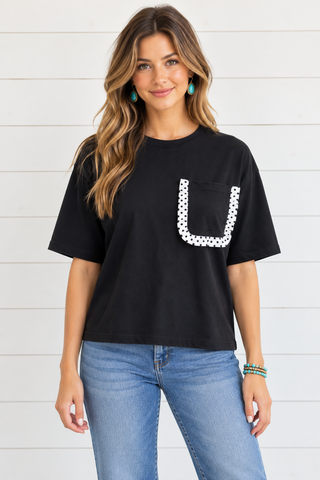 Female model wearing a black short sleeve tee with white polka dot ruffle trim around the chest pocket.