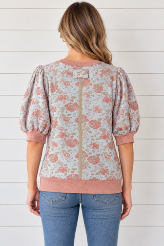Back view of a floral puff sleeve top with a contrasting center seam and dusty rose ribbed neckline, cuffs, and hem.