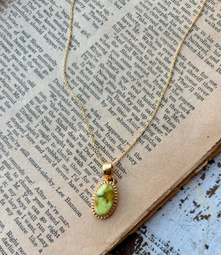 Oval yellow\-green Palomino turquoise pendant with a beaded gold border on a gold\-plated sterling silver chain, displayed on an open book\.