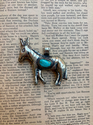 Western donkey pendant with an oval turquoise stone set in a detailed silver-tone donkey design, photographed on a vintage book page.