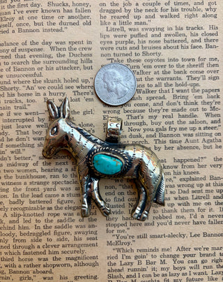 Western donkey pendant with an oval turquoise stone set in a detailed silver-tone donkey design, photographed on a vintage book page.