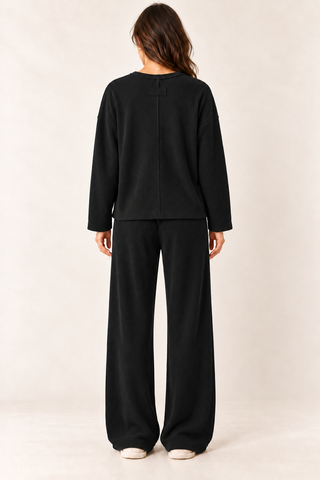 Model wearing a black waffle knit lounge set with a long\-sleeve crewneck top, chest pocket, and matching wide\-leg pants\.