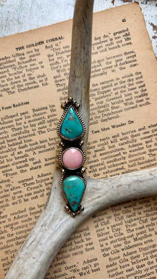 Adjustable pink conch and turquoise ring featuring a round pink conch center and two teardrop turquoise stones set in detailed antiqued alloy.