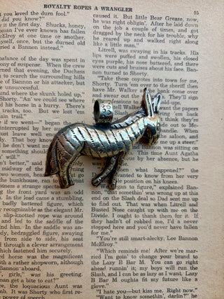 Western donkey pendant with an oval turquoise stone set in a detailed silver-tone donkey design, photographed on a vintage book page.