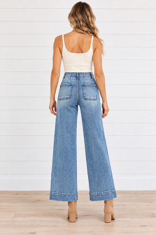 Back view of medium blue wide leg jeans with two patch pockets and wide stitched hems, styled with tan ankle boots.