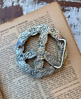 Back view of a peace sign statement belt buckle featuring ornate engraved alloy detailing and a metal belt loop.