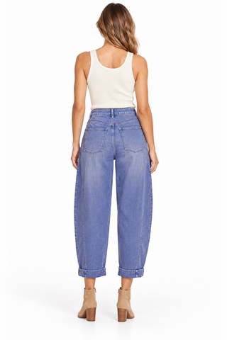 Front view of a model wearing faded Marlin blue barrel jeans with curved knee seams and rolled cuffs, styled with a cream tank and tan boots.