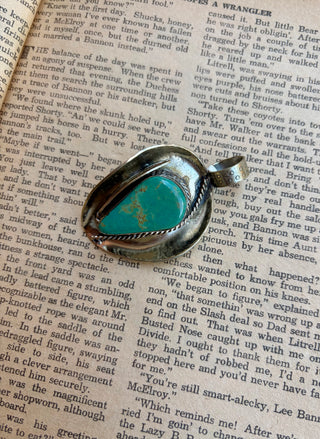 Cowboy hat pendant featuring a large teardrop-shaped turquoise stone with Southwestern rope detailing in an alloy setting.