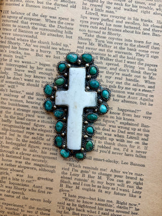 White cross pendant surrounded by turquoise stones with detailed Western-style metalwork.