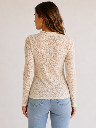 A woman shown from the back wearing a fitted long-sleeve lace top in a warm cream or light beige color, paired with light blue jeans, against a plain light gray studio background.
